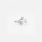 A delicate silver ring featuring three small star and flower and butterfly motifs set with clear stones, displayed on a clean white background with a soft reflection.